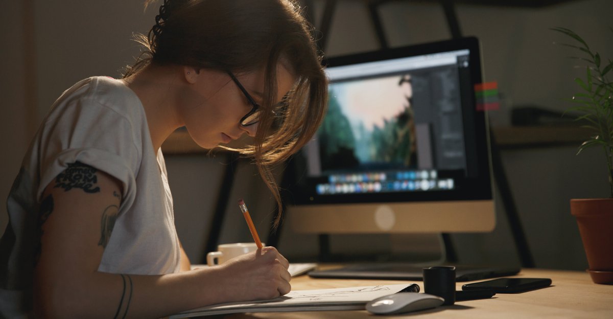 Graphic designer sketching ideas by hand with design software open in the background