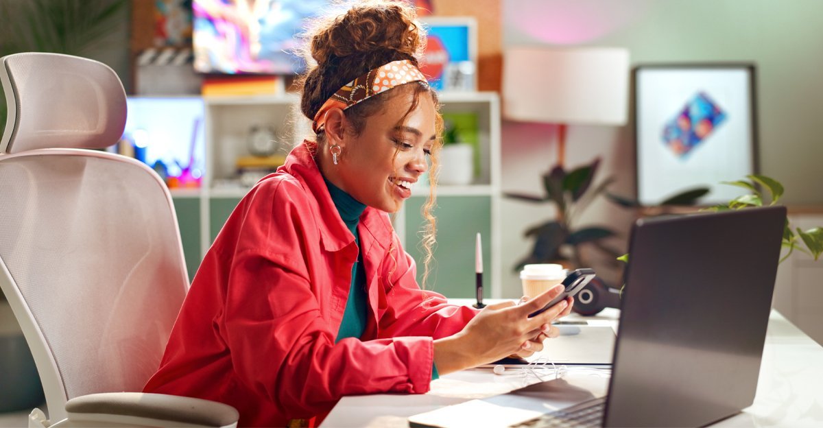 A woman smiling at her phone at a creative desk — how to brief a designer
