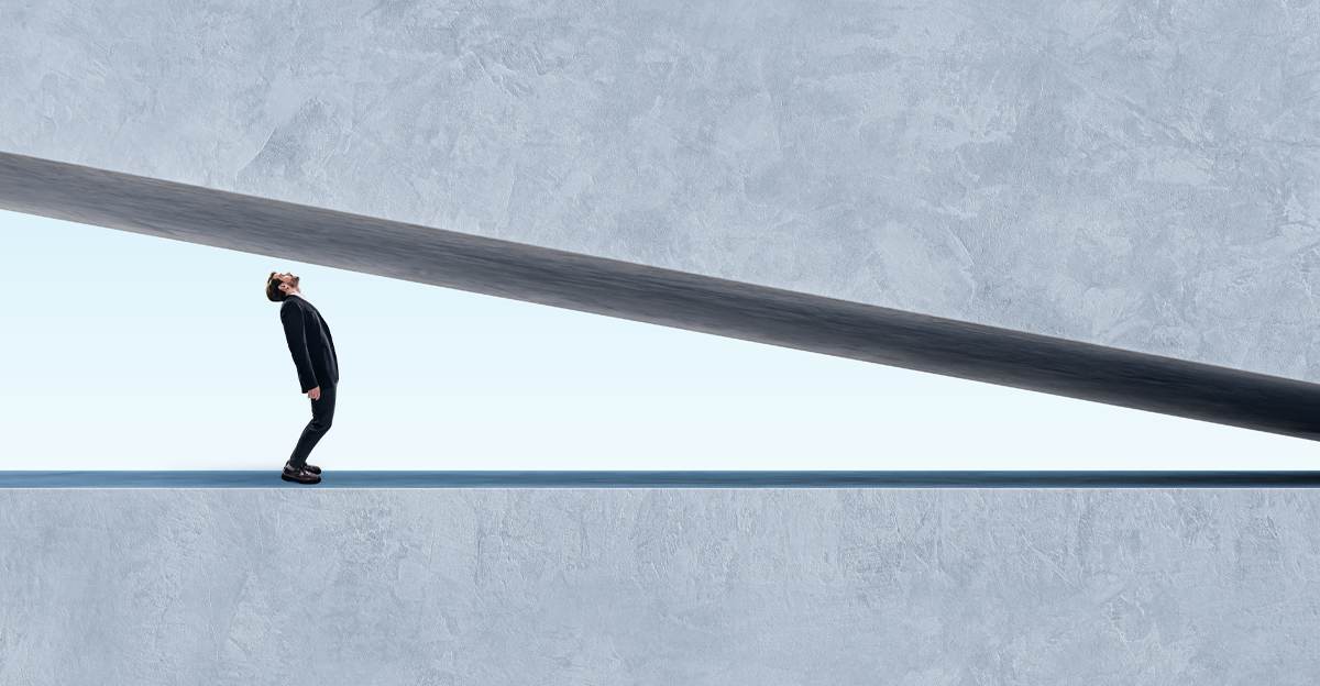 Person standing beneath a lowering beam representing the pressure of AI in graphic design